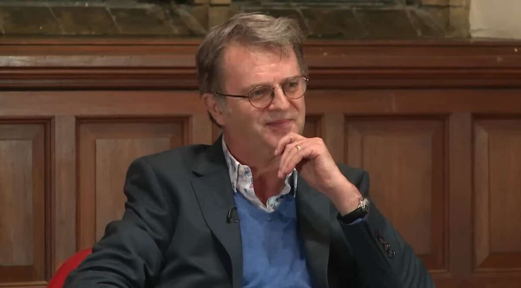 Paul Merton smiling while discussing a scene with a student at The Oxford Union