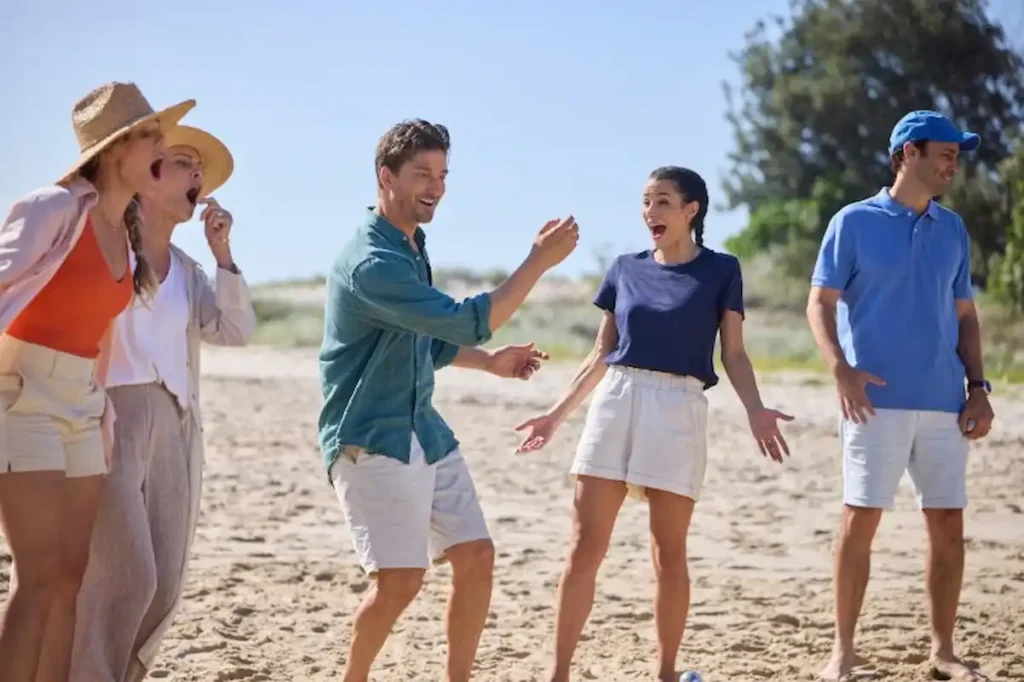 Aussie at Heart scene showing four people laughing and talking together on a sunny beach in Queensland, dressed in casual summer clothing