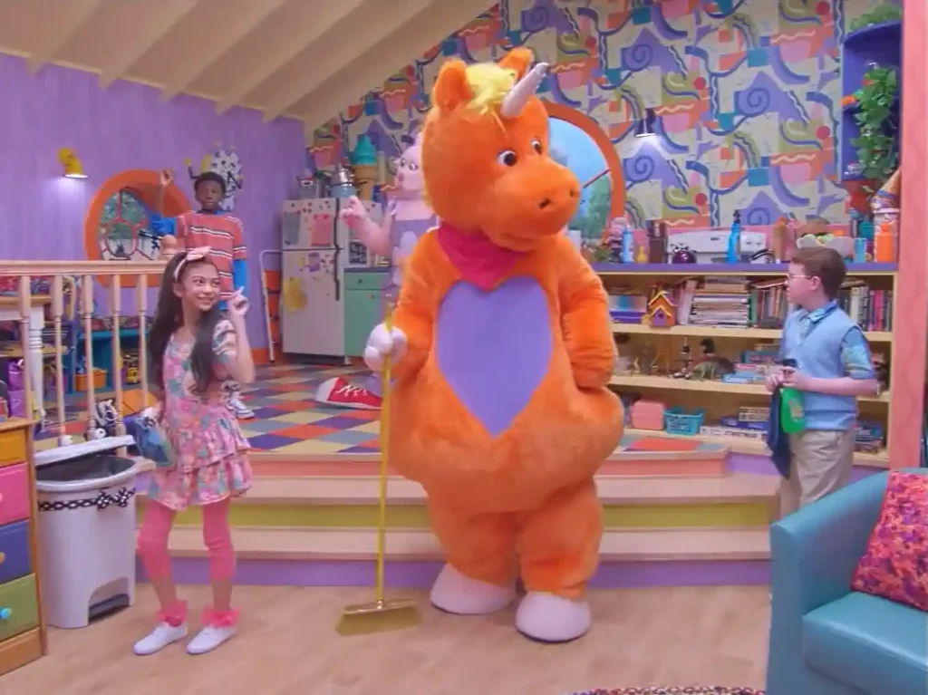 Orange unicorn character Buddy standing with two children inside a colorful classroom.